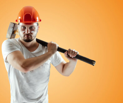 Bearded Man in a helmet holds a sledgehammer on an orange background. Concept of construction, contractor, repair.