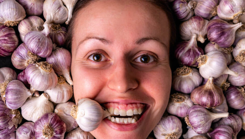 The girl holds a garlic bulb in her teeth. Portrait of a woman among many garlic bulbs