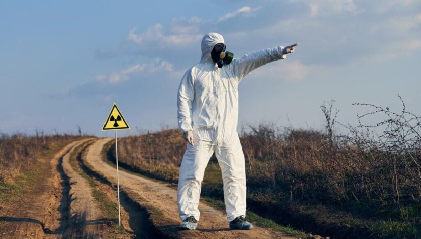 man-protective-coverall-gas-mask-standing-village-road-field-caution-sign_651396-2178