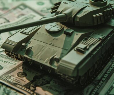 A small model tank is positioned on top of U.S. dollars, symbolizing the close relationship between finance and military power.