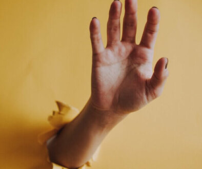 Vertical shot of a person's hand palm breaking through a yellow paper wall