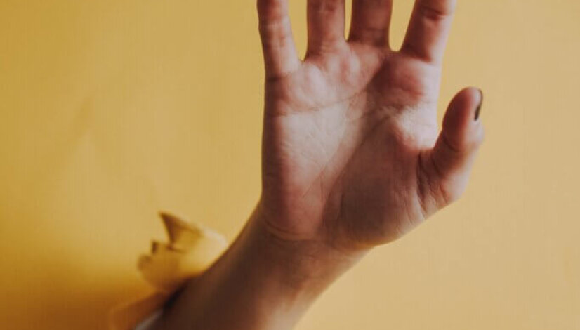 Vertical shot of a person's hand palm breaking through a yellow paper wall